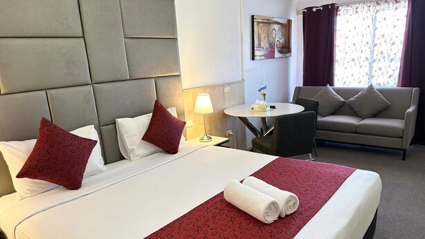 A hotel room with a large bed, a small round table, a sofa, and a painting on the wall.