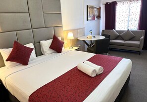 A hotel room with a large bed, a small round table, a sofa, and a painting on the wall. - Countryman Motor Inn (Cowra)