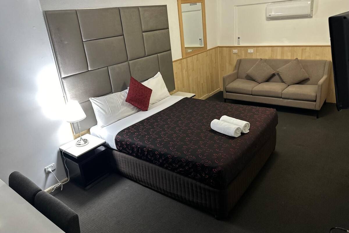 Ein Hotelzimmer mit Bett, Nachttisch mit Lampe, Sofa und Spiegel an der Wand.