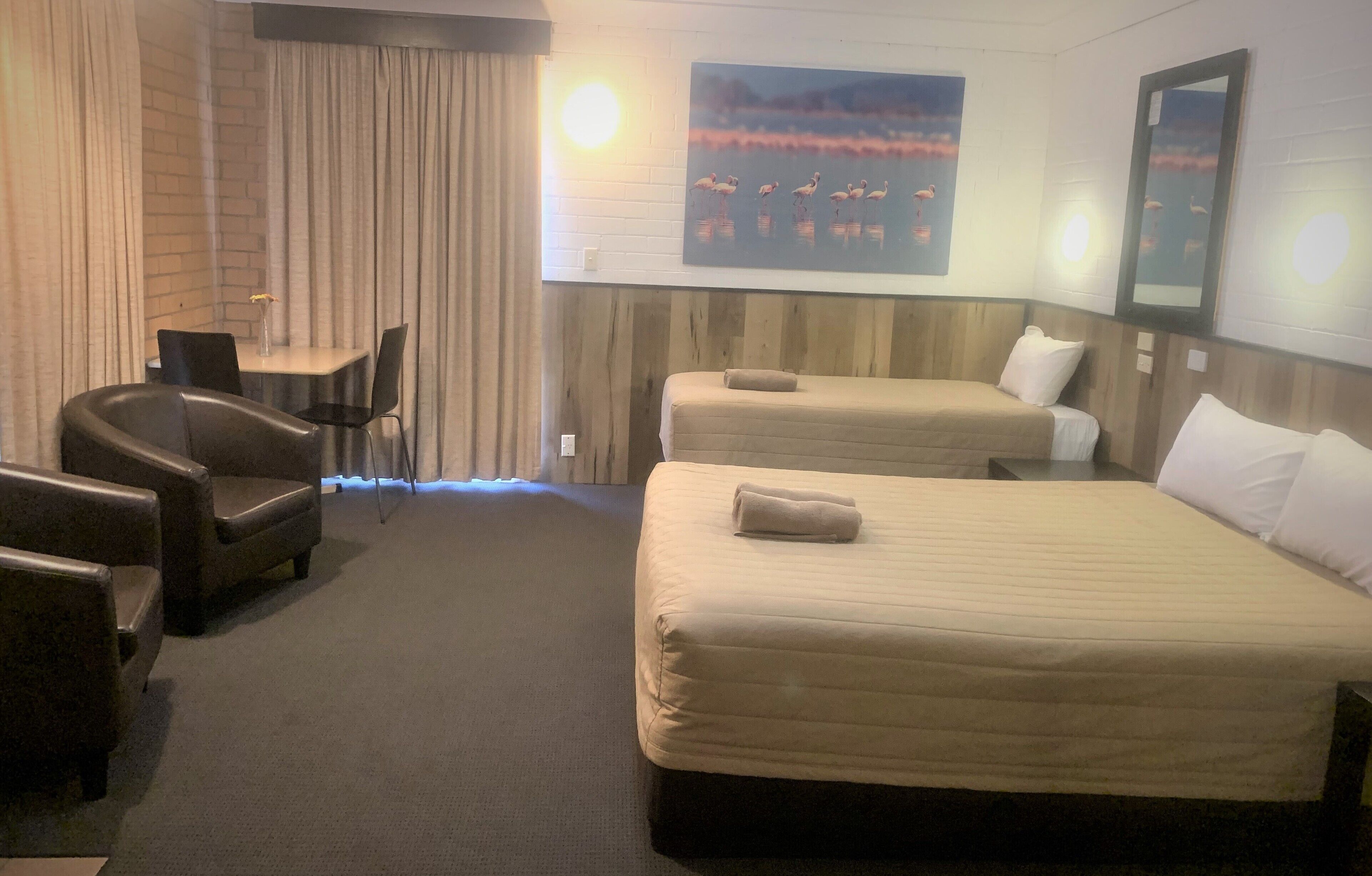A hotel room with two beds, a seating area with chairs, a small table, and a painting on the wall.