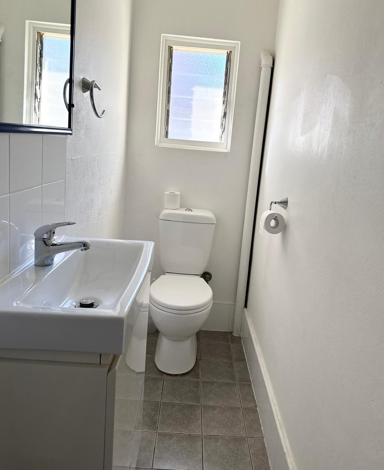 A small, clean bathroom with a white sink, toilet, and a window above the toilet.