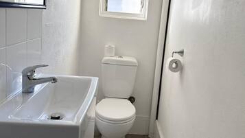 A small, clean bathroom with a white sink, toilet, and a window above the toilet.