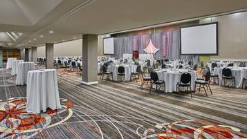 A large conference room with round tables, chairs, and a carpeted floor.