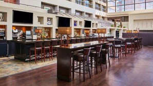 A spacious hotel lobby with a long bar area, multiple seating options, and a high ceiling with large windows. - Hyatt Regency Lexington (Lexington)