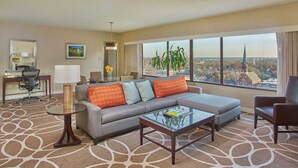 A hotel room with a large window offering a city view, a sofa with patterned cushions, a small table, and a desk with a chair. - Hyatt Regency Lexington (Lexington)