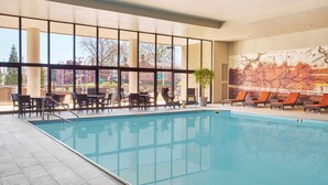 An indoor swimming pool with clear views of the outside, a mural on the wall, and a seating area with tables and chairs. - Hyatt Regency Lexington (Lexington)