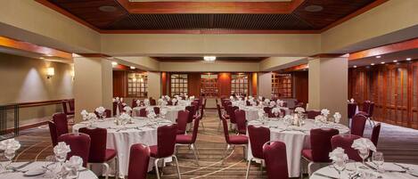 A banquet hall with round tables, red chairs, and white tablecloths.