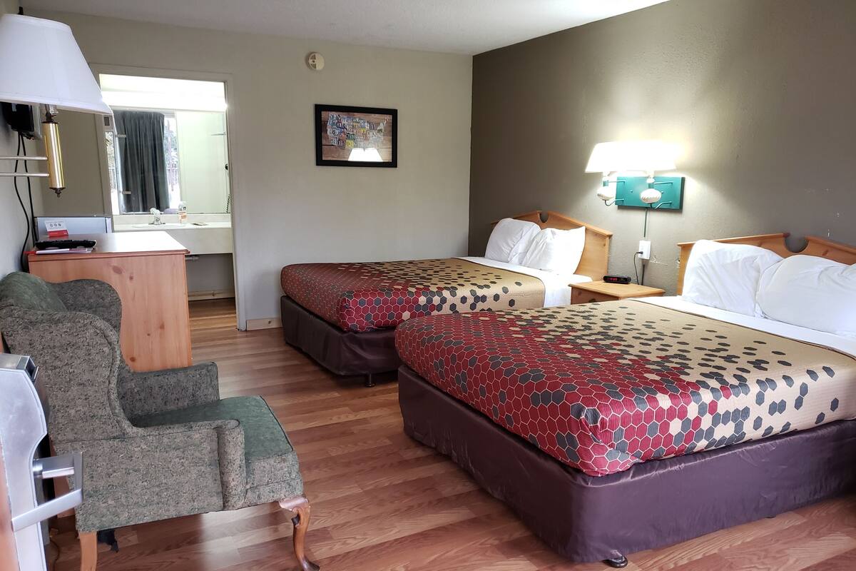 A hotel room with two beds, a desk, a chair, and a window.