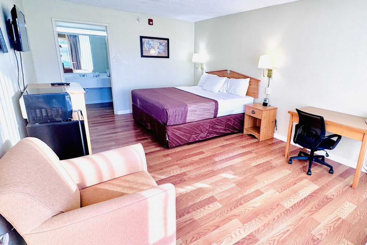 A hotel room with a bed, a desk with a chair, a sofa, a TV, and a telephone.