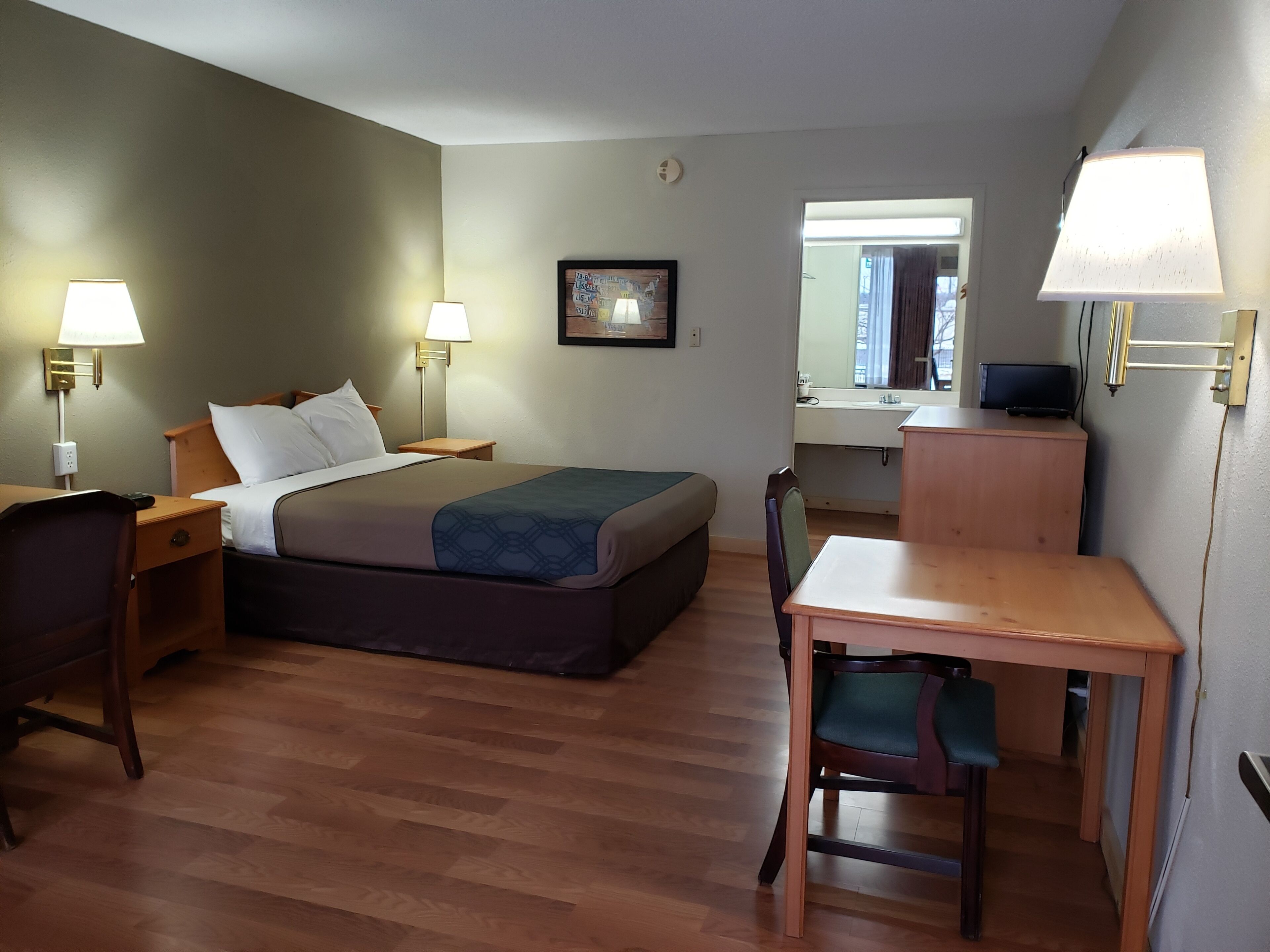 Una habitació d'hotel amb un llit, taules de nit, escriptori, cadira, mirall i televisió.
