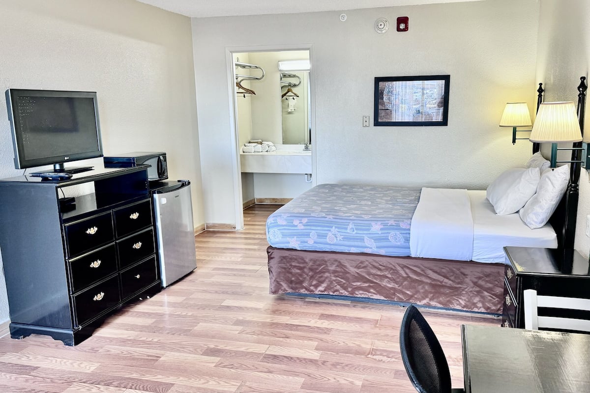 A hotel room with a bed, a desk with a computer, a TV, a lamp, and a chair.