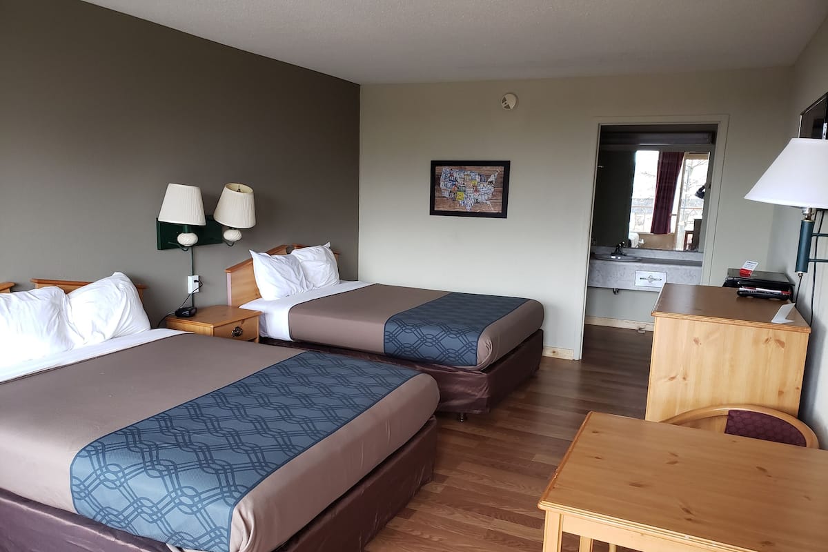 A hotel room with two beds, a desk, a mirror, and a wall-mounted lamp.