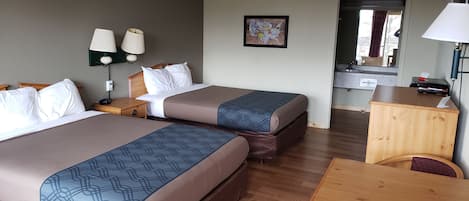 Une chambre d’hôtel avec deux lits, un bureau, un miroir et une lampe fixée au mur.