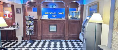 A hotel lobby with a check-in counter, a bulletin board with flyers, a clock, and a vending machine.