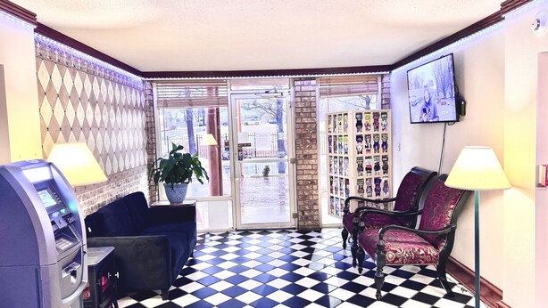 A lobby with a checkered floor, a seating area with chairs, a potted plant, a wall-mounted TV, and a bookshelf. - Mountain Home Inn (Mountain Home)