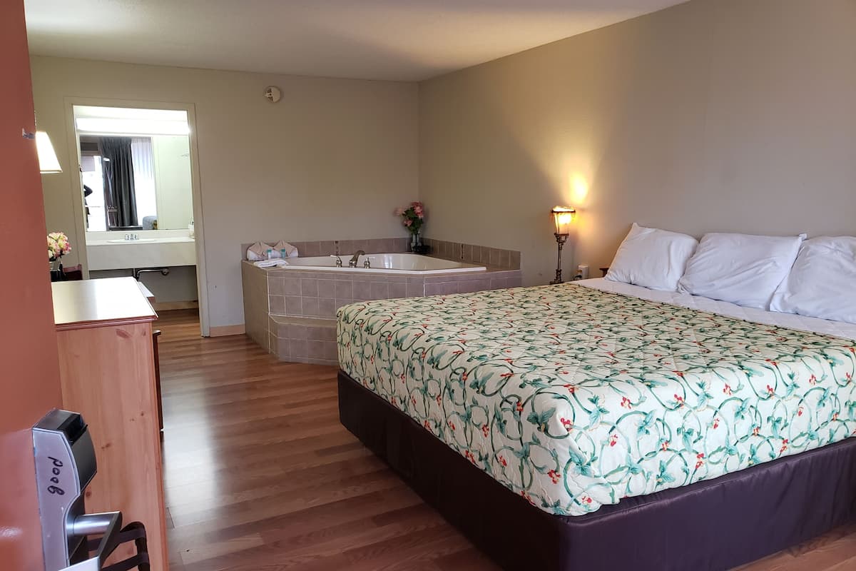 A hotel room with a large bed, a separate bathroom with a bathtub, and a desk with a chair.