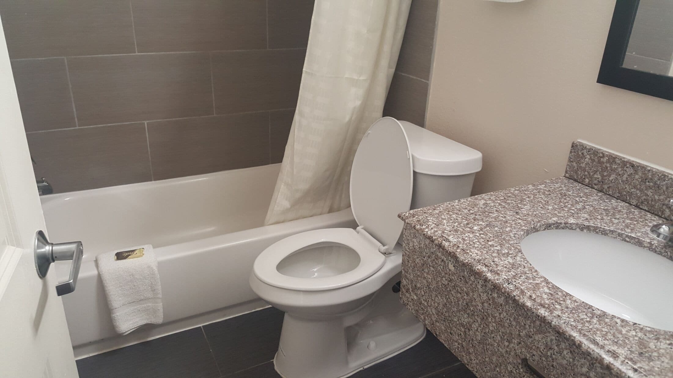 Un baño con inodoro blanco, bañera y encimera de granito con lavamanos.