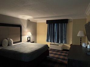 Ein Hotelzimmer mit Bett, Nachttisch, Lampe, Klimaanlage und Schreibtisch mit Stuhl.