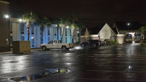 A parking lot with vehicles, a building with a unique triangular roof, and palm trees. - Regency inn and Suites (Pensacola)
