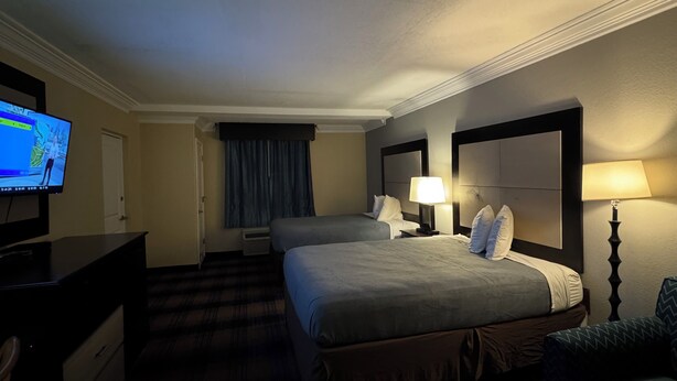 A hotel room with two beds, a desk, a television, and a lamp. - Regency inn and Suites (Pensacola)