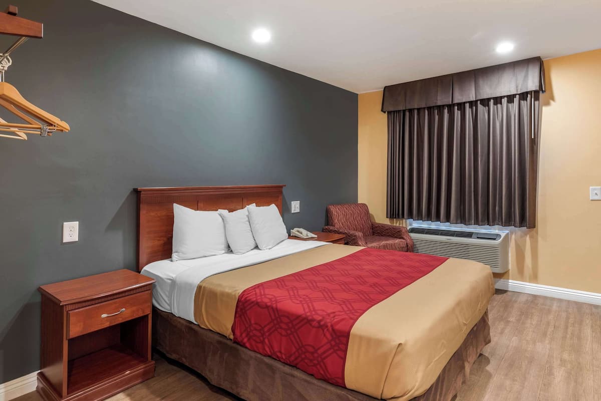 A hotel room with a bed, bedside table, chair, and window with curtains.