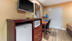 Ein Hotelzimmer mit einem Holztisch, einem Flachbildfernseher, einer Mikrowelle, einem Kühlschrank, einem Sessel und einem Bett.