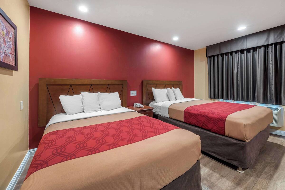 A hotel room with two beds, each with a red and beige bedspread, wooden headboards, white pillows, and a nightstand with a telephone.
