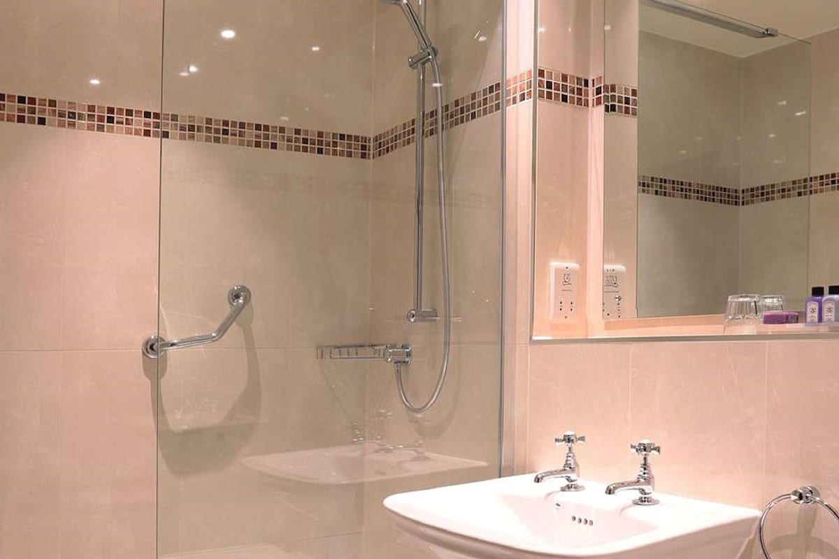 A modern bathroom with a glass-enclosed shower, a pedestal sink, and a large mirror.