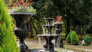 A multi-tiered fountain with water cascading down, surrounded by lush greenery and a stone pathway. - Macdonald Kilhey Court (Wigan)