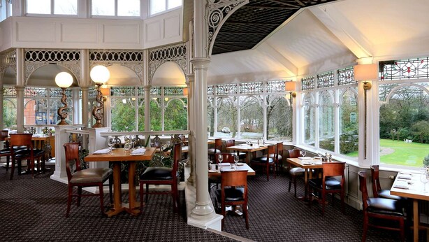 An indoor dining area with high ceilings, ornate columns, and large windows offering a view of the outdoors. - Macdonald Kilhey Court (Wigan)