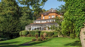 A large, multi-story house with a conservatory, surrounded by well-maintained gardens and trees. - Macdonald Kilhey Court (Wigan)
