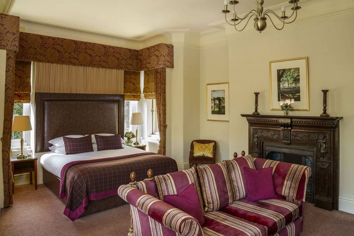 A hotel room with a large bed, a sofa, a fireplace, and framed pictures on the walls.