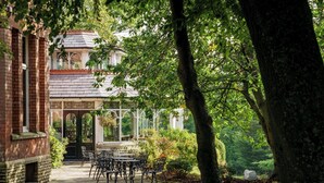 A brick building with a conservatory, outdoor seating, and lush greenery. - Macdonald Kilhey Court (Wigan)