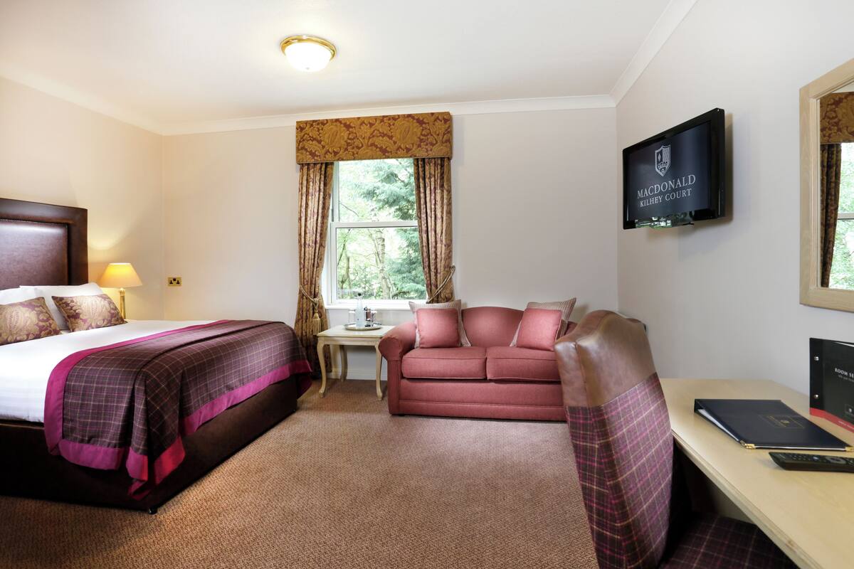 A hotel room with a bed, a desk, a sofa, and a television on the wall.