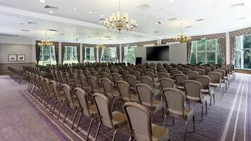 Una sala conferenze con file di sedie, un grande schermo e lampadari.