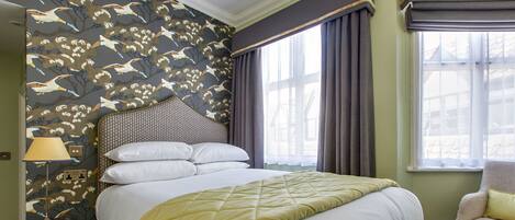 Un lit bien fait, recouvert d’une courtepointe, une chaise avec un coussin, une lampe sur une table d’appoint et une fenêtre avec des rideaux.