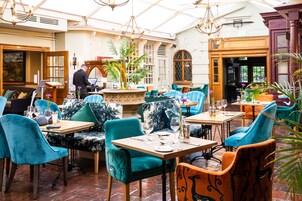 Un restaurante con sillas tapizadas en tonos aguamarina y naranja, mesas de madera y una planta en el centro.