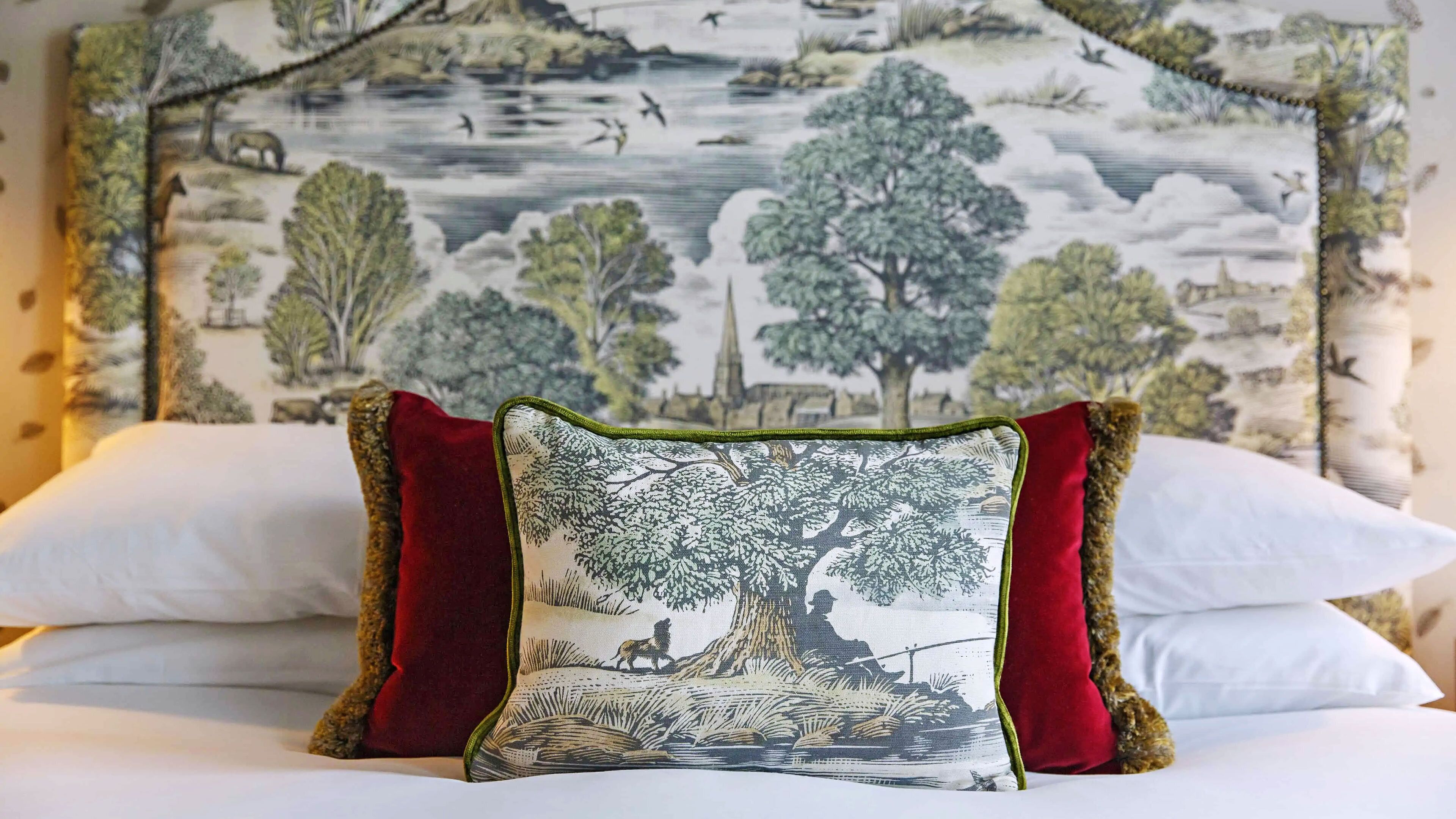 A bed with white linens, a red pillow, and a pillow with a nature scene.