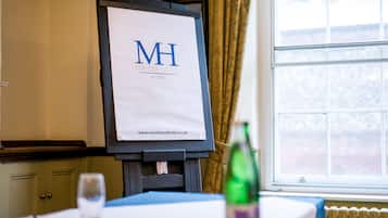 A room with a large window, a framed sign on the wall, and a table with a glass and a bottle.