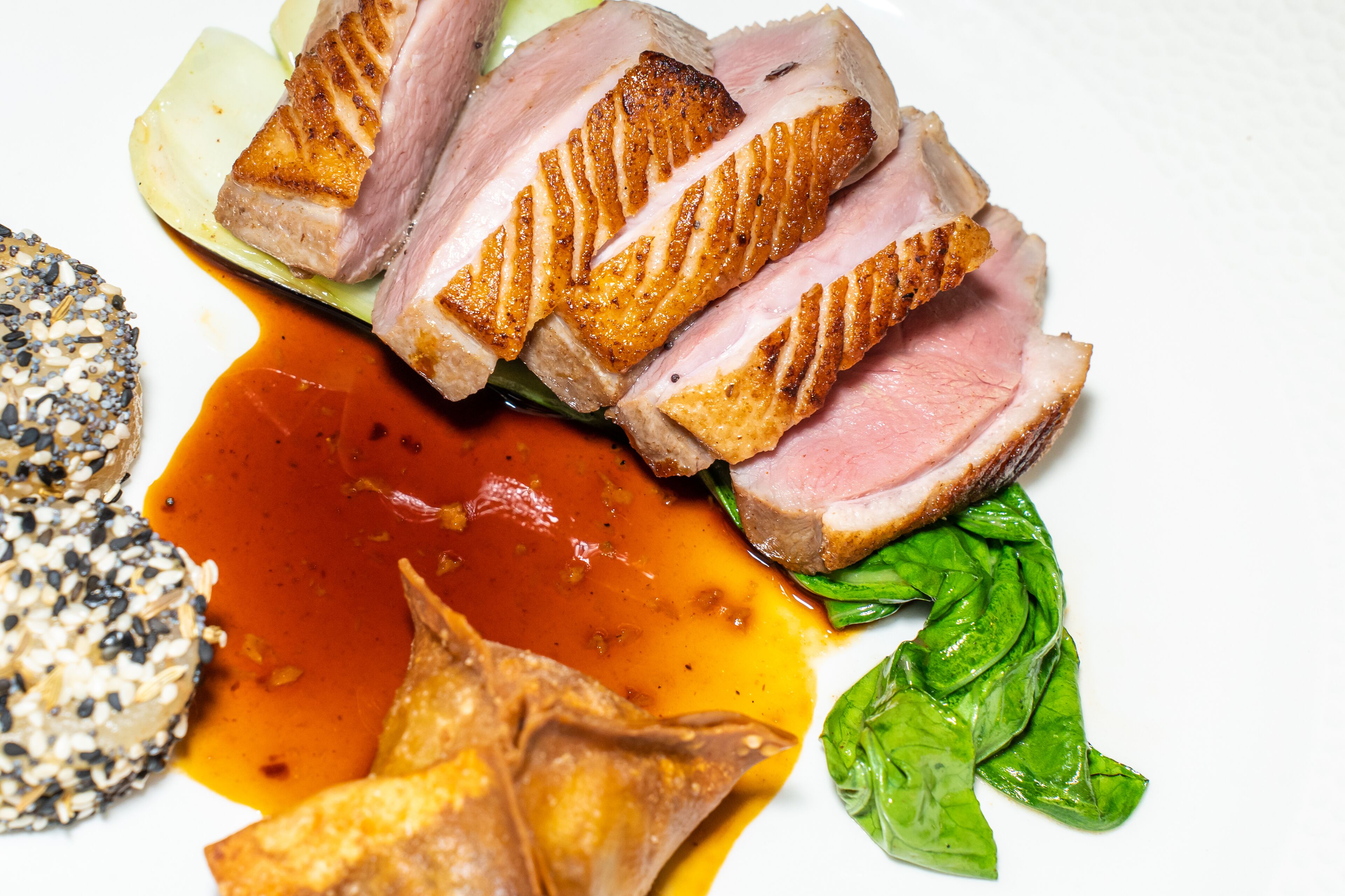 A plate with sliced meat, sauce, and greens.