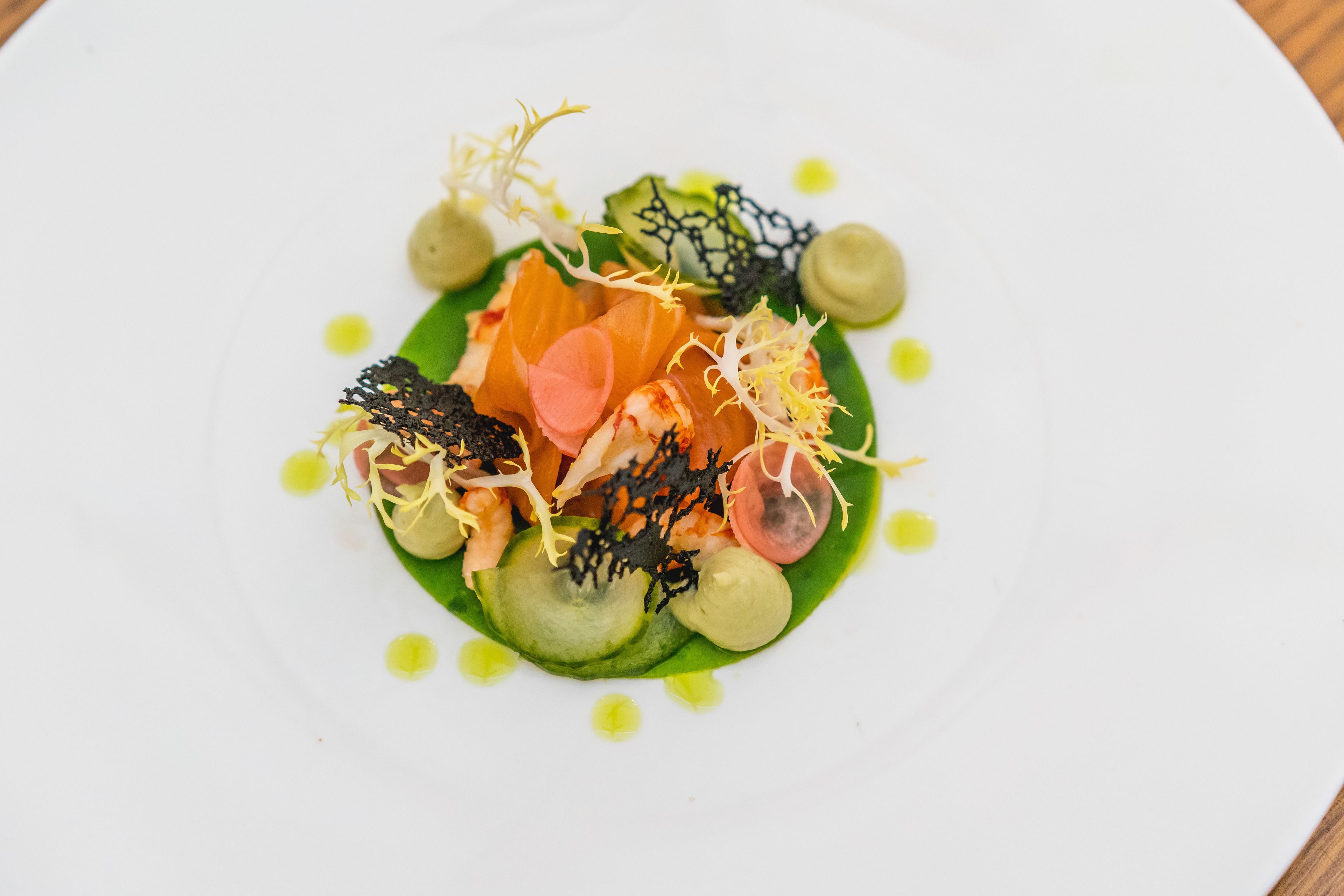 Ein weißer Teller mit einer Portion Essen, darunter Lachs, Gemüse und Garnituren.