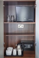 Un mueble de madera con una computadora portátil, dos botellas de vidrio, una tetera y una cafetera.