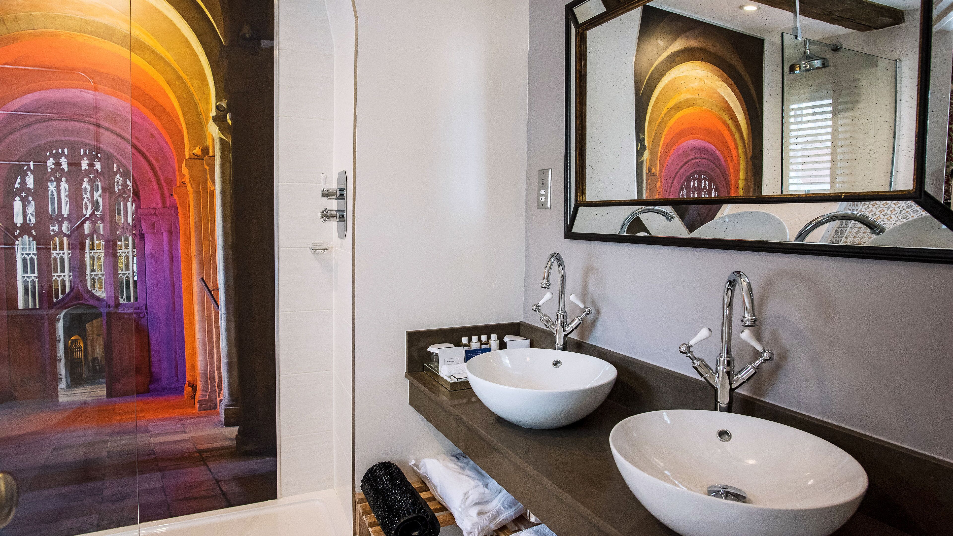 A bathroom with two white sinks, a mirror, and a shower.