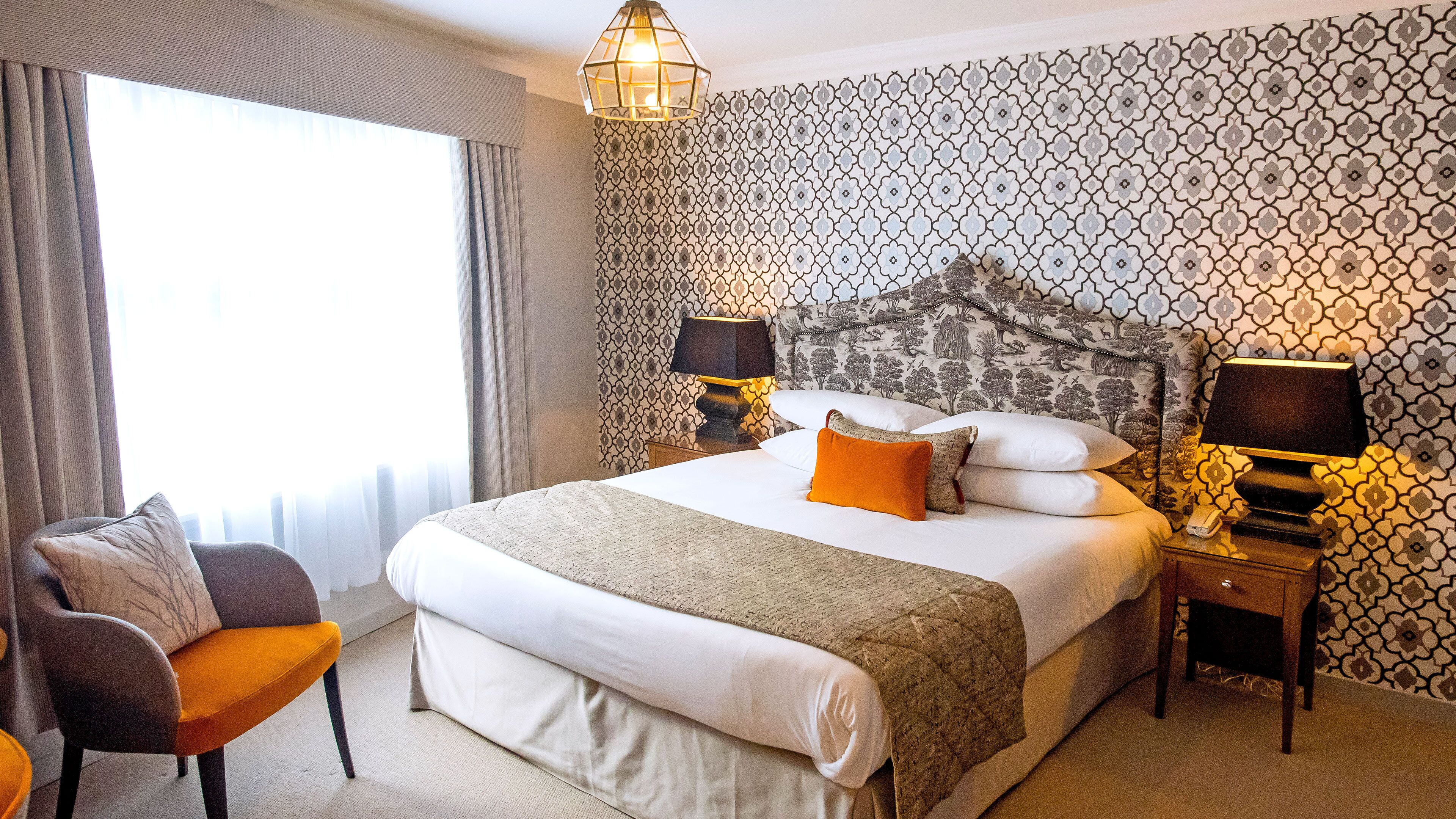 Ein Hotelzimmer mit einem großen Bett, zwei Nachttischlampen, einem Sessel und einer Wand mit Muster.