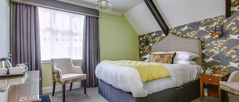 Un dormitorio con una cama grande, una silla, un escritorio con una bandeja de objetos y un papel tapiz estampado.