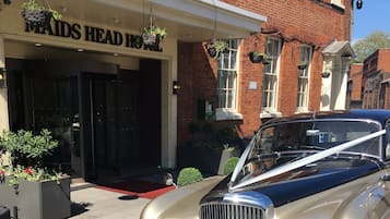 A classic Rolls Royce parked in front of a hotel with a red carpet leading to the entrance.