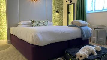 A modern bedroom with a large bed, a pet bed, a wall-mounted light, and a mirror.