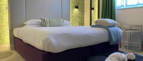 Un dormitorio moderno con una cama grande, una cama para mascotas, una lámpara de pared y un espejo.