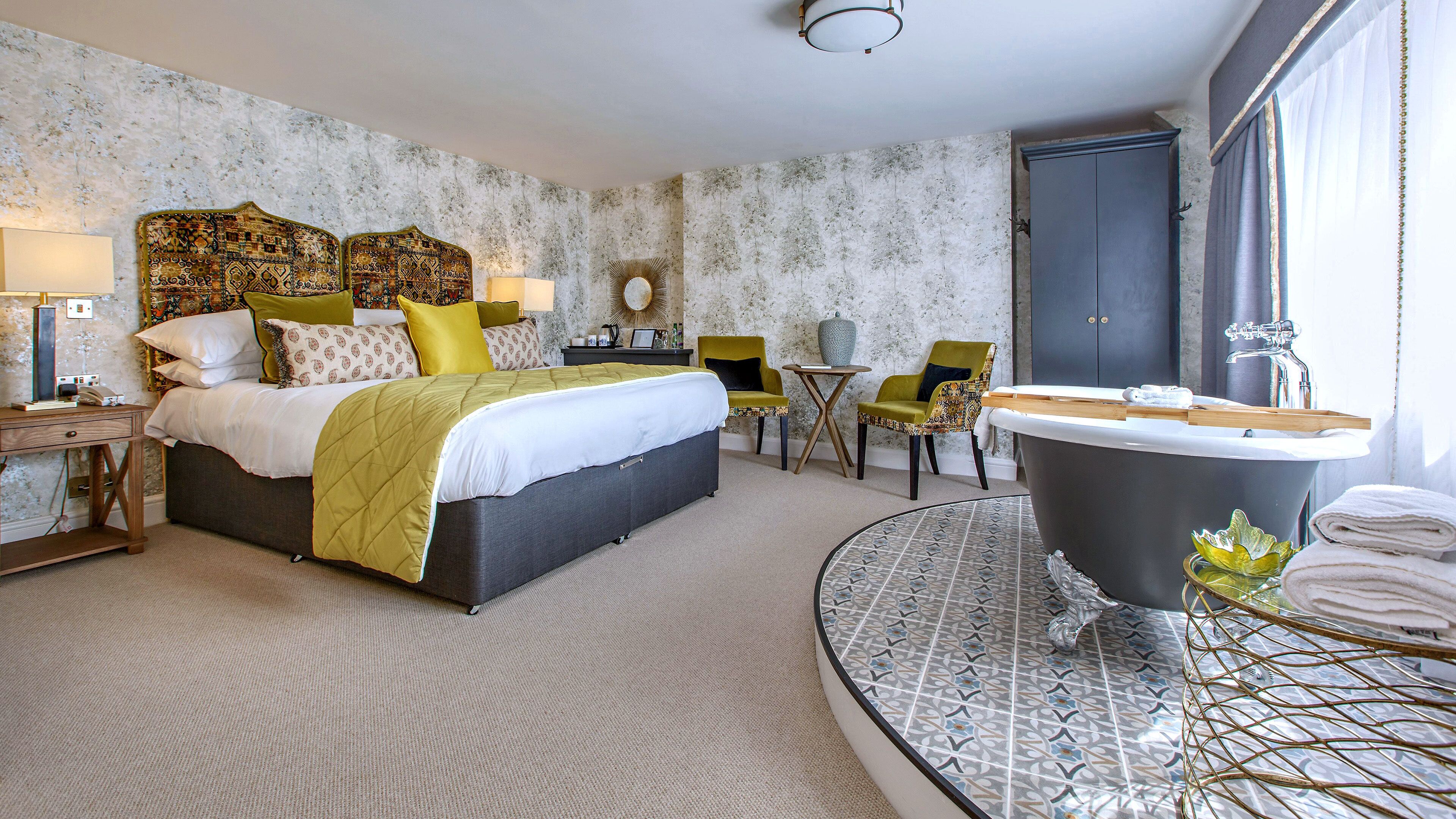 A hotel room with a bed, a round bathroom with a bathtub, a small table, two chairs, and a mirror.