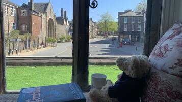 A window view of a street with buildings, a teddy bear, and a book on a windowsill.